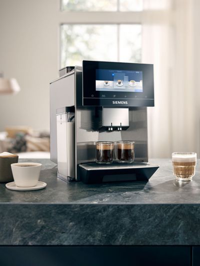 A Siemens coffee machine dispensing two espressos, surrounded by various coffee drinks on a countertop in a modern living space.