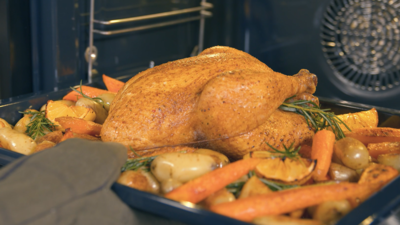 Ganzes H&auml;hnchen mit Kartoffeln und Karotten auf Backblech im Garraum eines Siemens iQ700 Backofens.