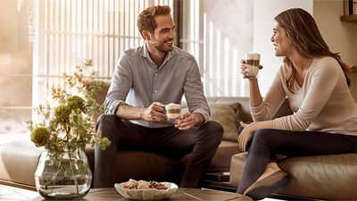 A smiling couple enjoying coffee and conversation on a sofa in a bright living room.