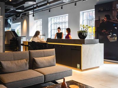 Three women converse at a modern kitchen island with under-cabinet lighting in a showroom or office lounge, with a grey sofa in the foreground.