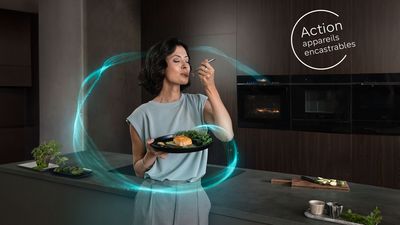 Une femme se tient devant un four encastrable iQ700. Elle tient dans sa main une assiette avec un plat de saumon et une fourchette.   
