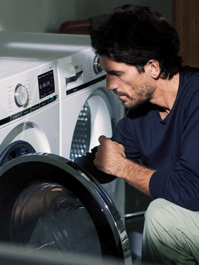 A man holding up a freshly washed patterned shirt in a laundry room with a washer and dryer.