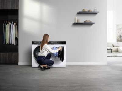 Eine Frau l&auml;dt W&auml;sche in einen wei&szlig;en Siemens Trockner mit schwarzer T&uuml;r f&uuml;r perfekte Trocknungsergebnisse.