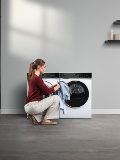 Een vrouw laadt een gekleurde kledingstukken in een Siemens wasmachine.