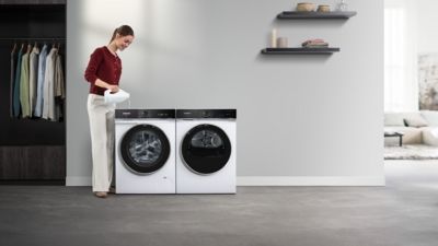 Vrouw vult een Siemens wasmachine met wasmiddel uit een fles. 