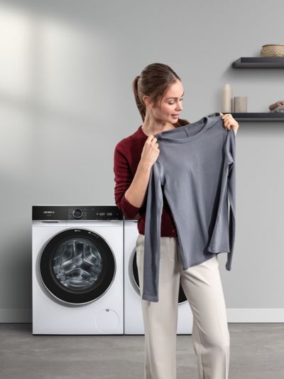  Vrouw houdt een grijs shirt omhoog, met op de achtergrond een Siemens wasmachine.