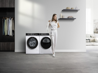 Eine Frau l&auml;dt W&auml;sche in einen wei&szlig;en Siemens Trockner mit schwarzer T&uuml;r f&uuml;r perfekte Trocknungsergebnisse. 