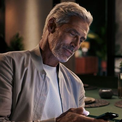 Homme avec cheveux boucl&eacute;s assis sur le canap&eacute; en utilisant smartphone dans le salon.