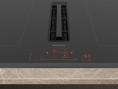 A black Siemens induction cooktop with an integrated downdraft extractor, featuring red digital controls displaying cooking settings and a timer, set into a light marble countertop.