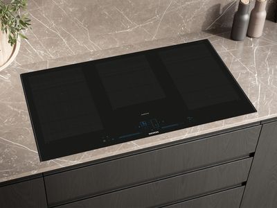 A black Siemens studioLine induction cooktop with multiple flexible cooking zones and blue digital controls, integrated into a dark marble-patterned countertop.