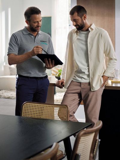 A service technician in a grey polo shirt showing a customer information on a tablet in a modern kitchen.