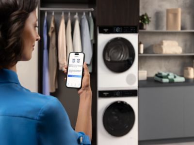 Vrouw bekijkt haar wasmachine in de Siemens Home Appliances-app in een moderne wasruimte.