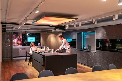 Cucina moderna con eleganti mobili, una grande isola di cottura ed elettrodomestici, con una persona che prepara il cibo in primo piano.