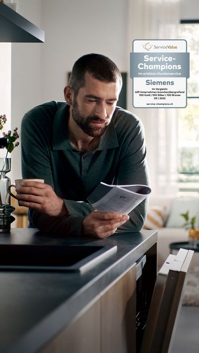 Ein Mann lehnt sich an die K&uuml;chentheke, h&auml;lt eine Tasse Kaffee und liest die Anleitung seines offenen Siemens Geschirrsp&uuml;lers