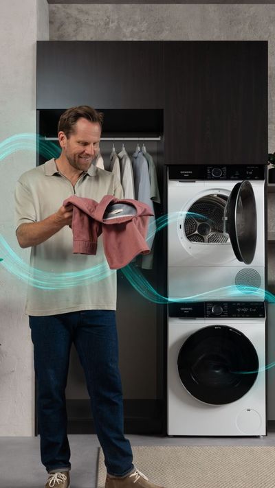 Een man kijkt naar wasgoed voor een Siemens iQ700-wasmachine in een lichte, moderne wasruimte.