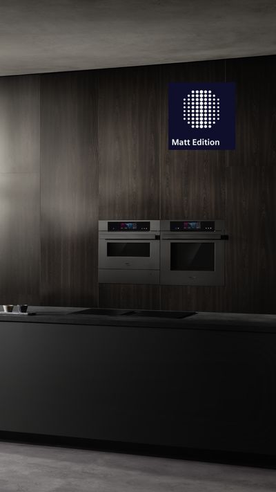 Questa cucina moderna &egrave; caratterizzata da una raffinata isola di colore nero, con un elegante rubinetto e forni Siemens integrati in una parete in legno scuro ravvivata dalle tonalit&agrave; di verde delle piante decorative.
