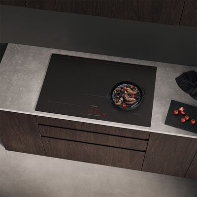 
         Une &eacute;l&eacute;gante table de cuisson &agrave; induction noire avec une po&ecirc;le de viande gr&eacute;sillante, entour&eacute;e de vapeur, et des citrons frais sur une planche &agrave; d&eacute;couper &agrave; proximit&eacute;.
        