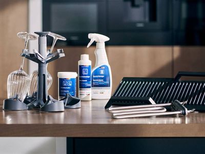 A collection of Bosch dishwasher accessories and cleaning products, including a wine glass holder, descaler, cleaner, and grill rack parts, displayed on a wooden countertop.