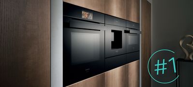       Strakke zwarte Siemens toestellen zijn elegant ingebouwd in een donkere, gestructureerde wand in deze moderne keuken, sfeervol versterkt door een gloeiend designelement.     