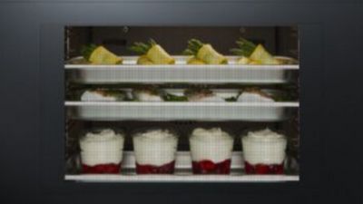 Three different dishes cooking simultaneously on separate shelves inside an oven: vegetable rolls, fish fillets, and layered fruit and cream desserts.