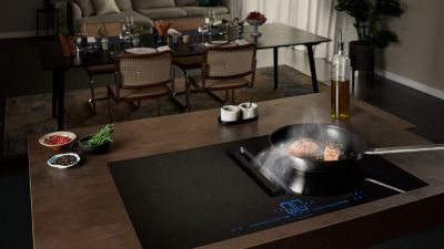 Cucina moderna con piano cottura a induzione, padella per cucinare e tavolo da pranzo con sedie e stoviglie sullo sfondo.