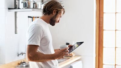 Мужчина с чашой кофе использует мобильное приложение Home Connect для настройки стиральной машины