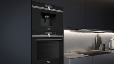 Cucina in nero con forno disposto in verticale e macchina del caffè integrata nel mobile alto.