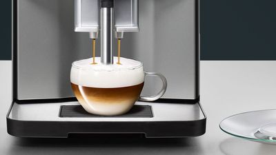 Eine Tasse Cappuccino wird mithilfe eines Kaffeevollautomaten zubereitet