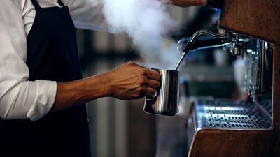 Ein Barista-Kaffeeprofi schäumt Milch für einen leckeren Kaffee auf