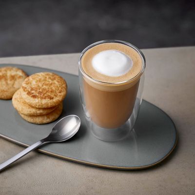 Eine Tasse mit Flat White Kaffee auf einem Teller mit Gebäck und Löffel