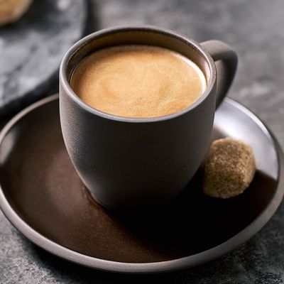Italienischer Mokka Kaffee ist in einer Dunklen Tasse mit einem Stück Würfelzucker und Gebäck auf einem Teller angerichtet