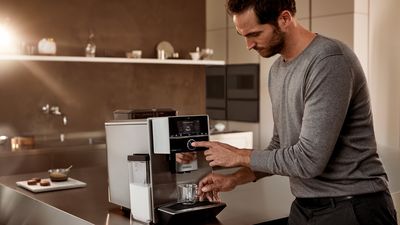 Ein Mann betätigt den Schalter einen Siemens Kaffeemaschine. Er schaltet die Kaffeemaschine ein.