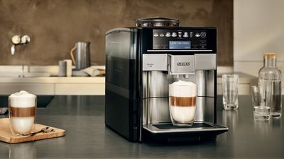 Une machine à café automatique Siemens EQ6 avec un café au lait fraîchement préparé sous la buse d'écoulement.