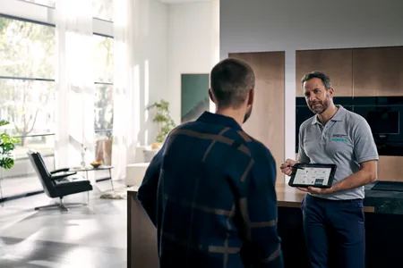 Siemens Kundendienst-Techniker erklärt einem Kunden die Gerätefunktionen auf einem Tablet in moderner Wohnküche.