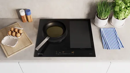 Encimera de cocina con placa de inducción, utensilios de cocina, huevos y plantas en macetas.