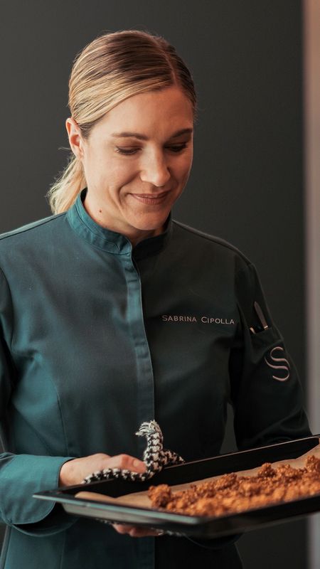 Eine Köchin in grüner Uniform zeigt ein Tablett mit frischem Gebäck – ein Ausdruck ihres Könnens und Feingefühls.