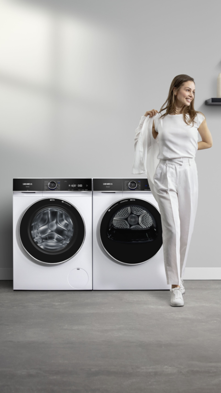 Siemens iQ700 Waschmaschine und Trockner nebeneinander, mit Model in weißem Outfit im modernen Raum.