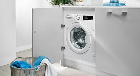 Lavadora Balay integrada bajo encimera, puerta abierta y cesta con toallas azules