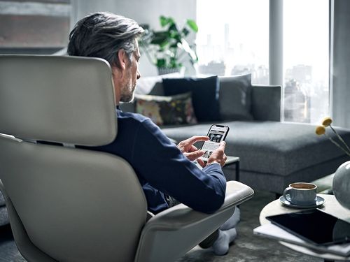Ein Mann sitzt in einem Sessel und bedient sein Smartphone.