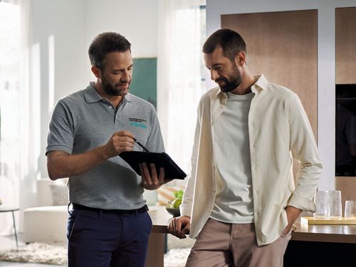 Un tecnico di assistenza Siemens mostra qualcosa a un cliente su un tablet in una cucina moderna e accogliente