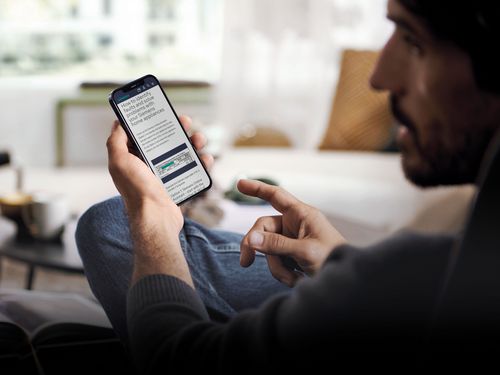 En person sitter bekv&auml;mt och h&aring;ller en smartphone som visar en webbsida om fels&ouml;kning av hush&aring;llsapparater.