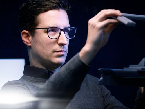 Een persoon in een verduisterde kamer bekijkt een strak, modern object met een innovatief ontwerp, dat getuigt van creativiteit en aandacht voor detail.