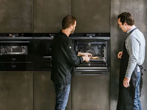 Zwei Männer begutachten hochwertige Siemens Einbaugeräte, welche sich in einer Küchenzeile befinden.