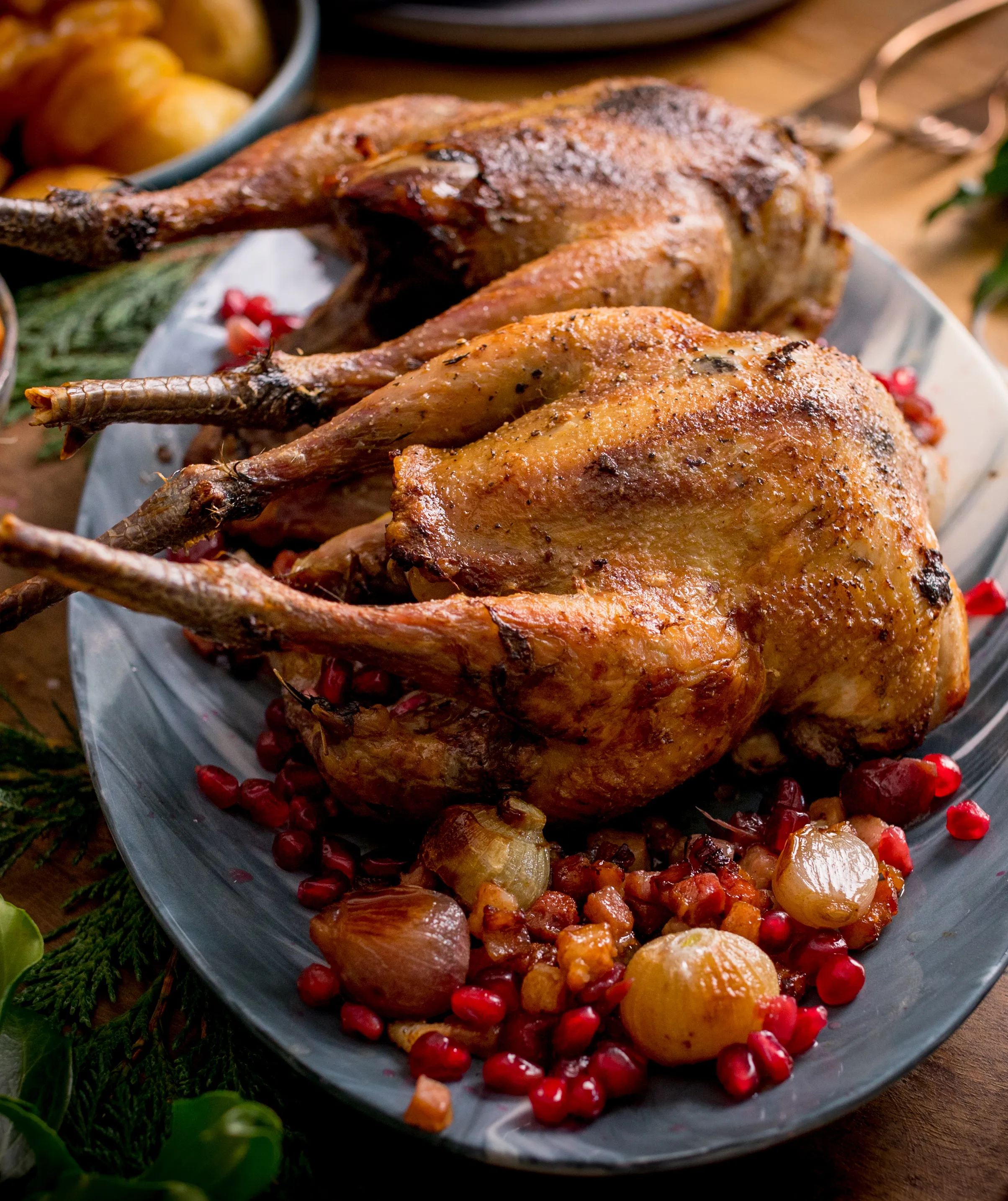 Roasted whole chicken on a plate, garnished with pomegranate seeds and herbs, accompanied by roasted potatoes.
