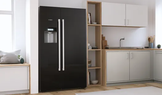 Black freestanding Bosch fridge with two large doors in a modern kitchen flooded with light.