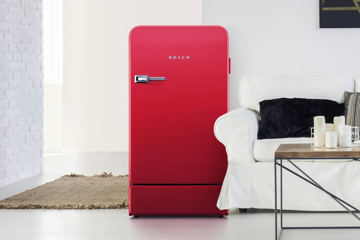 Red freestanding Bosch fridge in a modern room next to sofa and coffee table.