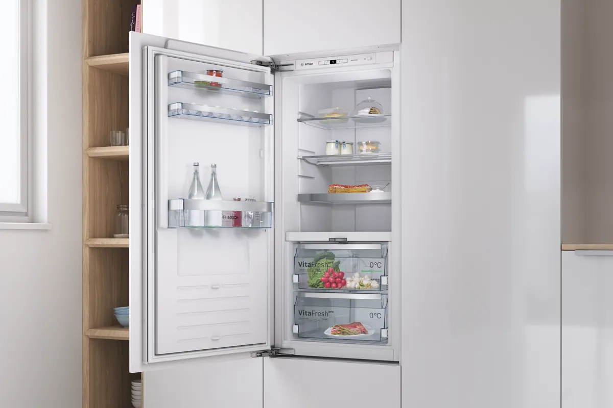 Built-in Bosch fridge with open door reveals fresh food and drinks inside. 