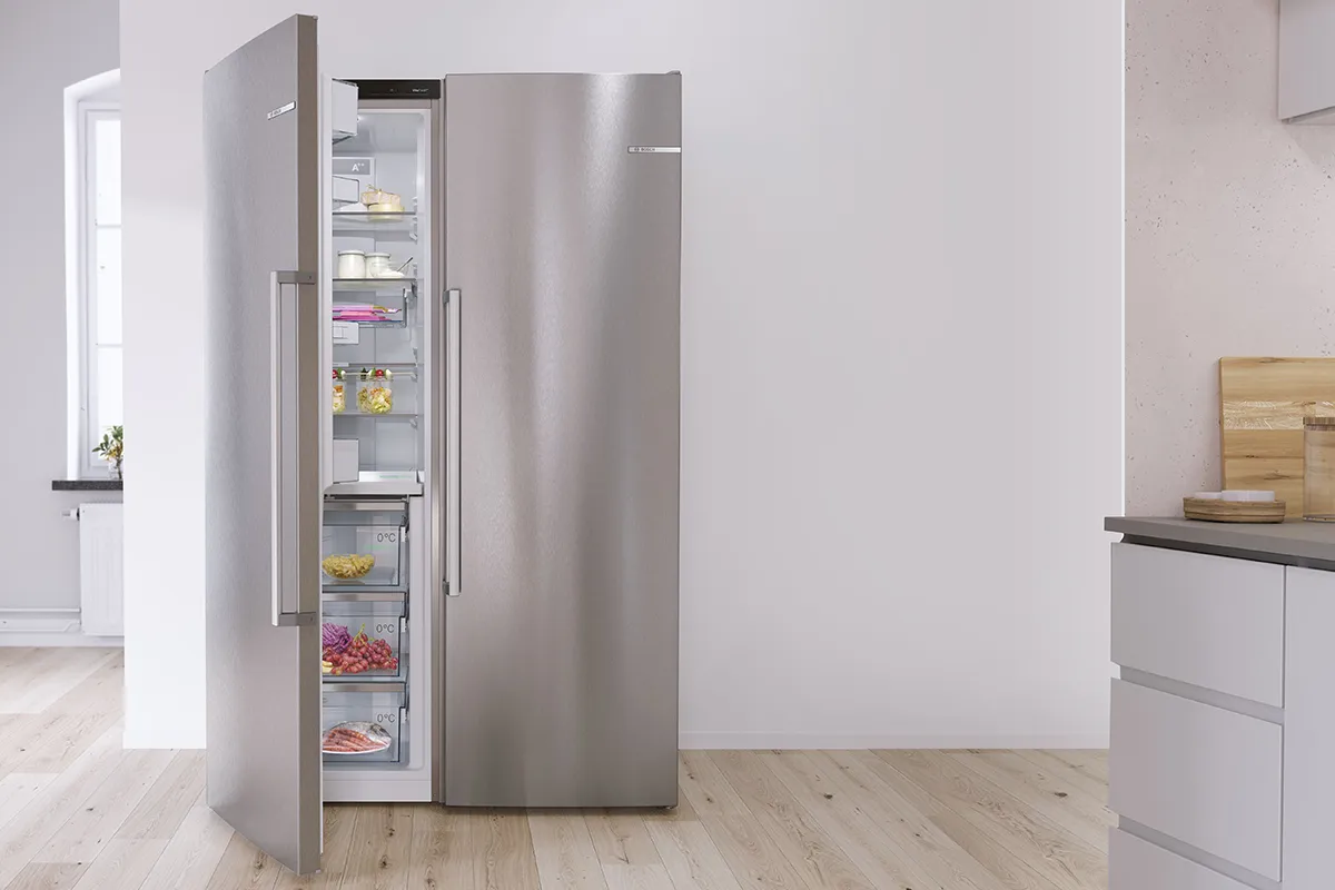 Silver freestanding side-by-side Bosch fridge in a white kitchen. Open door shows fresh food.