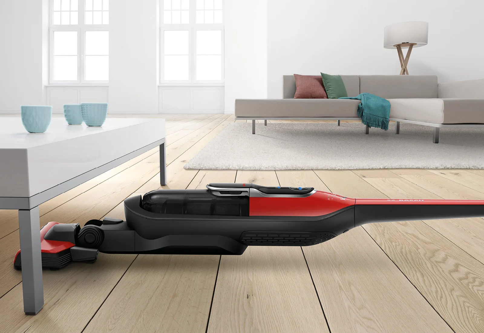 Living minimalist cu mobilier modern, podea din lemn dur, și un aspirator roșu și negru în prim-plan.