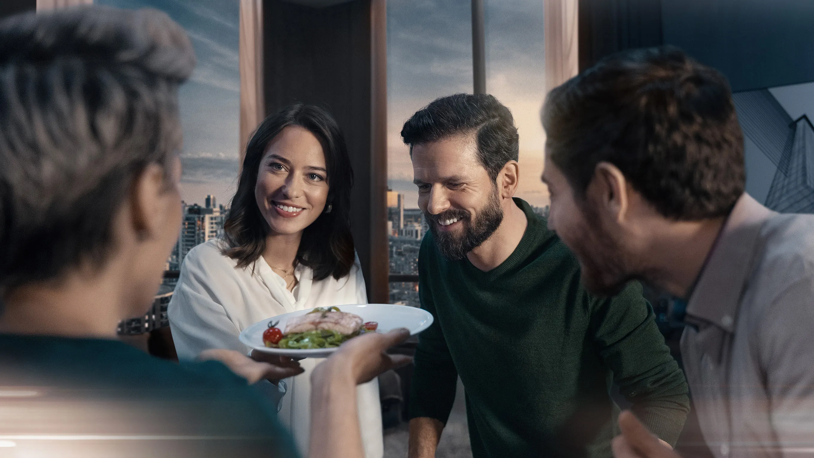 Group of friends enjoying a meal together in a modern setting with a city view.